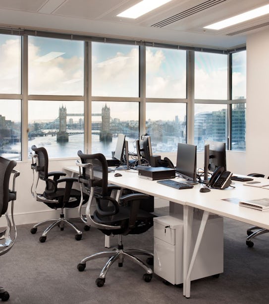 An office space with desks, chairs and monitors and view of Tower Bridge