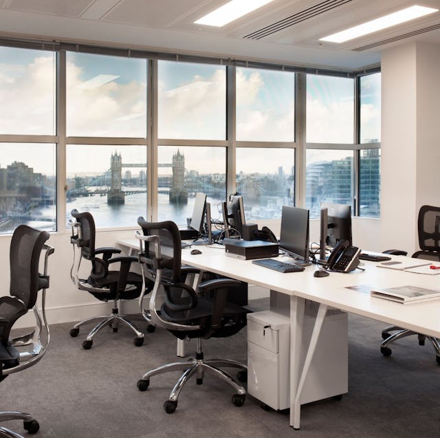 An office space with desks, chairs and monitors and view of Tower Bridge